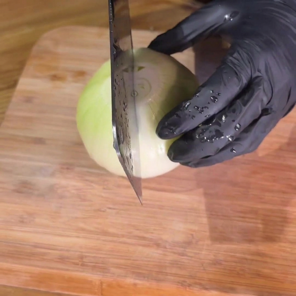 Zwiebeln werden sorgfältig in gleichmäßige Streifen auf einem Holzschneidebrett geschnitten.