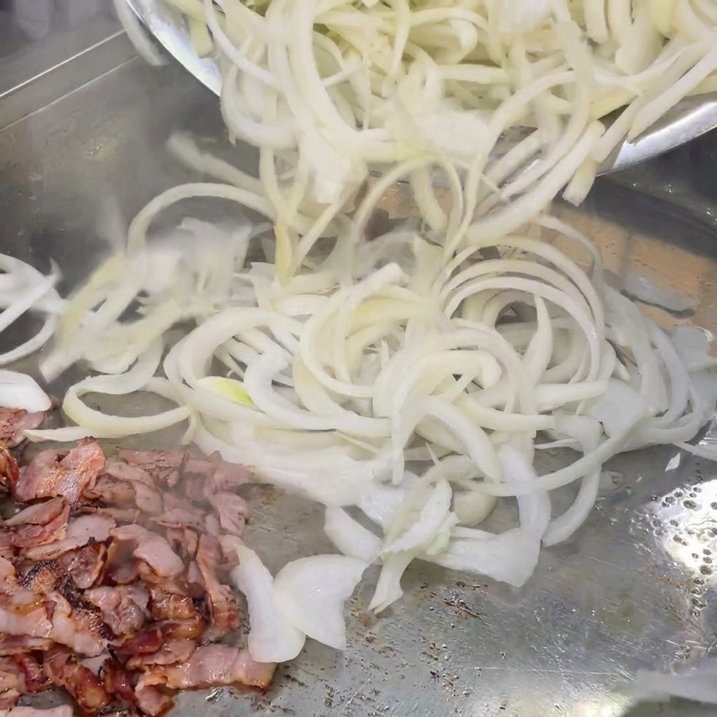 Frisch geschnittene weiße Zwiebeln werden mit gebratenen Speckstücken auf dem Grill vermengt.