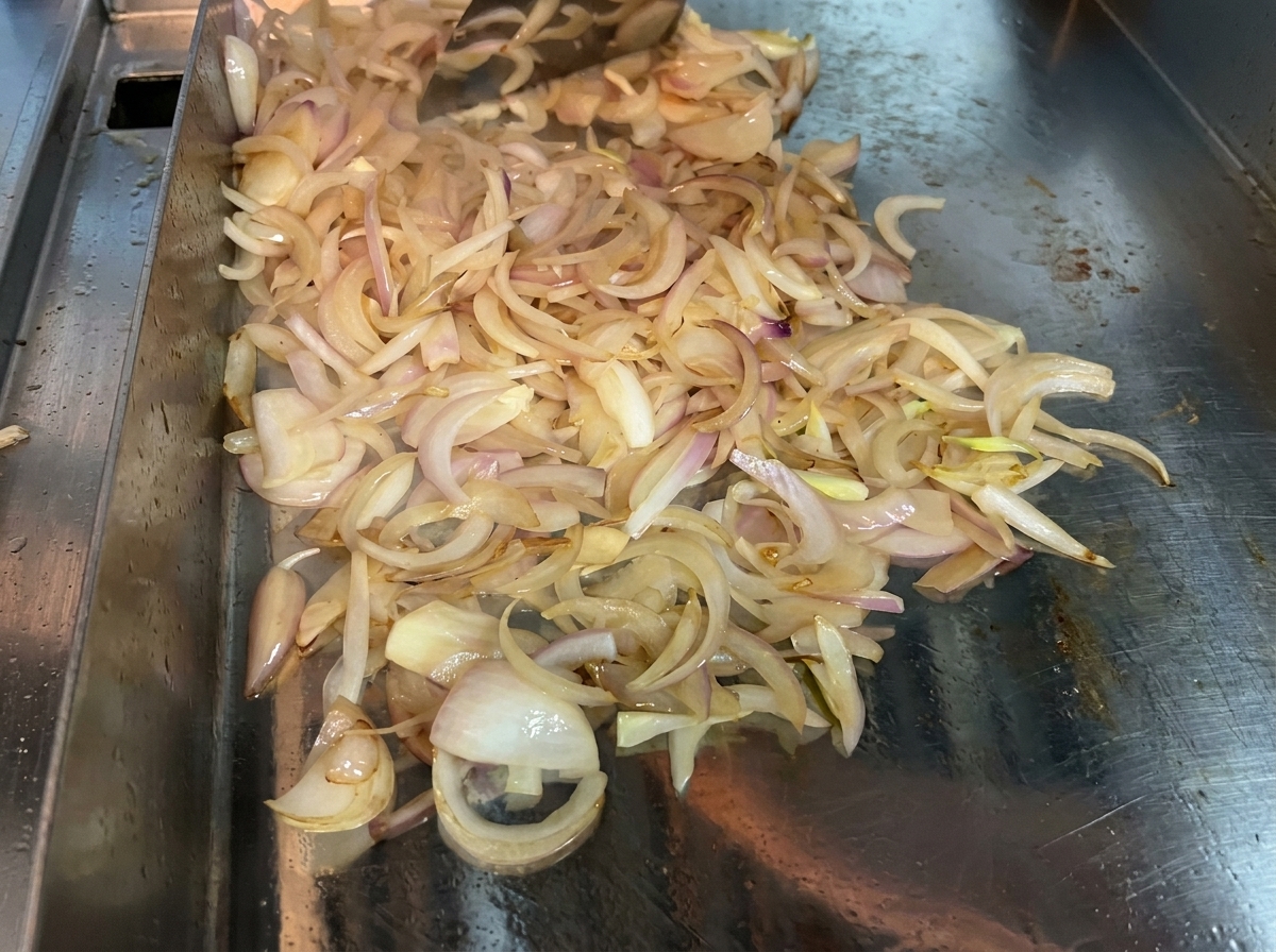 Geschnittene Zwiebeln werden in einer heißen Pfanne kontinuierlich gewendet, um sie weich und karamellisiert zu bekommen.