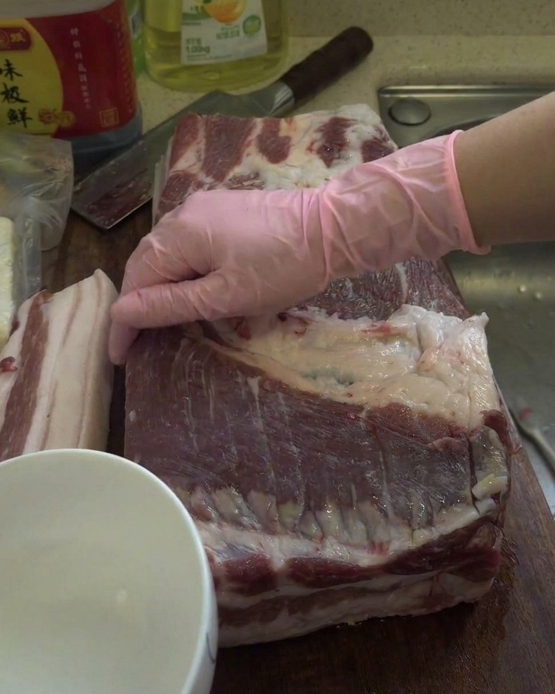 Ein rohes Stück Schweinebauch wird auf einem Holzbrett mit weißem Schnaps eingerieben.