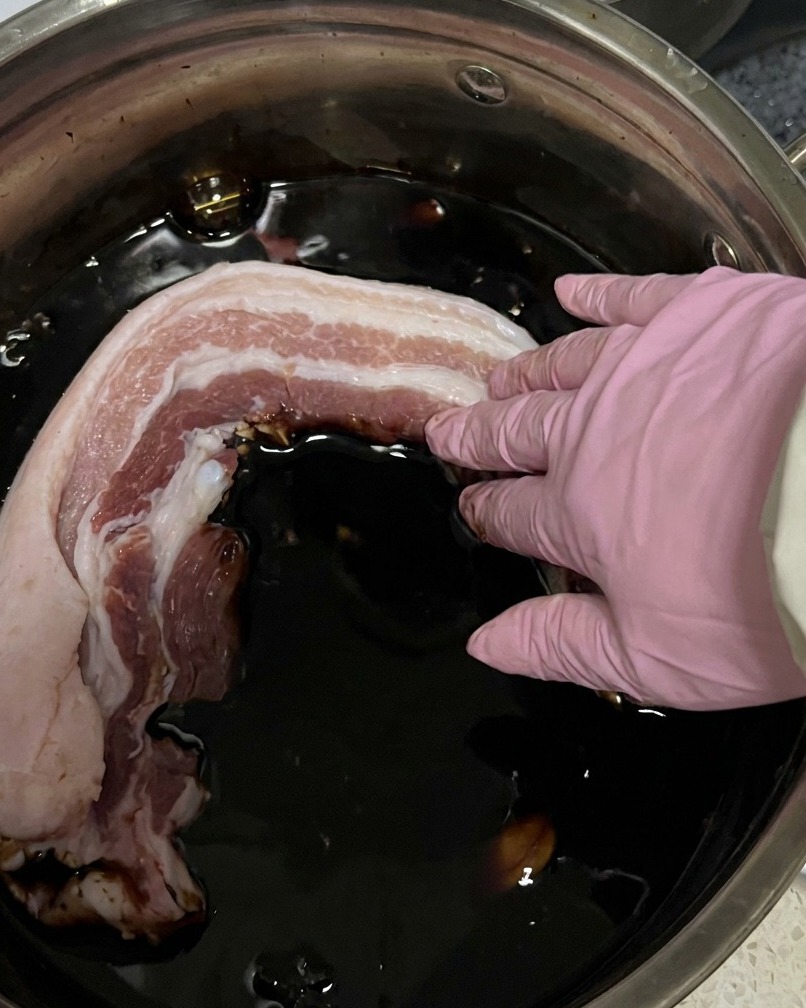 Rohe Fleischstreifen liegen in einem Topf und sind von dunkler Sojasaucen-Marinade bedeckt.