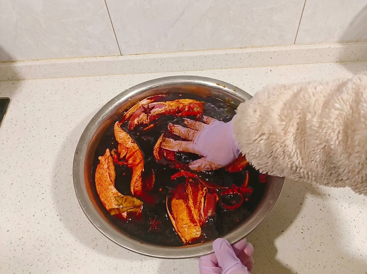 Behandschuhte Hände wenden die Schweinebauchstücke in einer Schüssel mit dunkler Marinade.