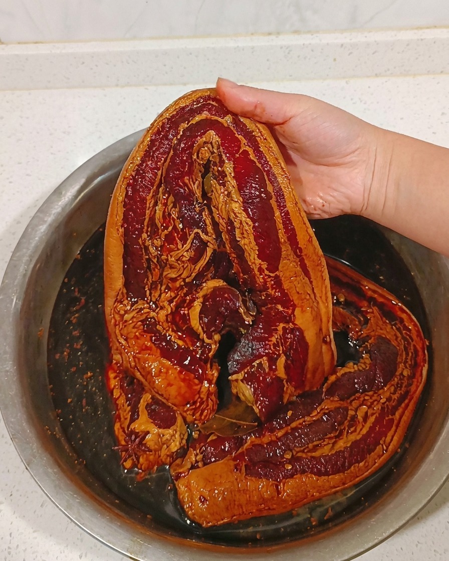 Ein Stück marinierter Schweinebauch wird unter warmem Wasser abgespült.