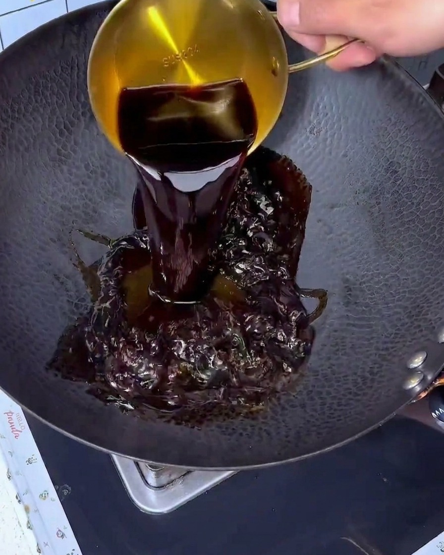 Sojasauce wird aus einem goldenen Messbecher in einen großen schwarzen Wok gegossen.