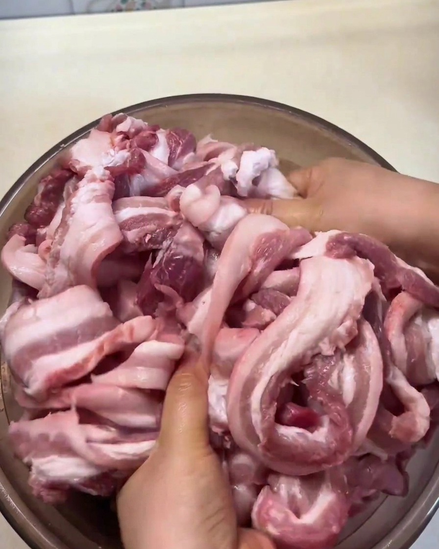 Rohe Schweinebauchstreifen werden von Hand mit Gewürzen und Marinade in einer großen Schüssel massiert.