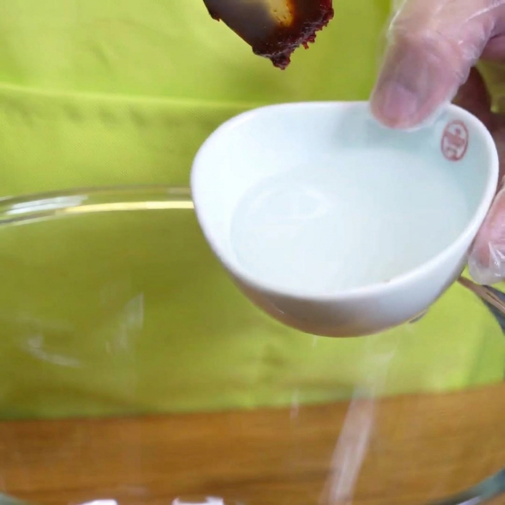 Dicker Stärkesirup tropft von einem Löffel in eine Schüssel mit Marinadenzutaten.