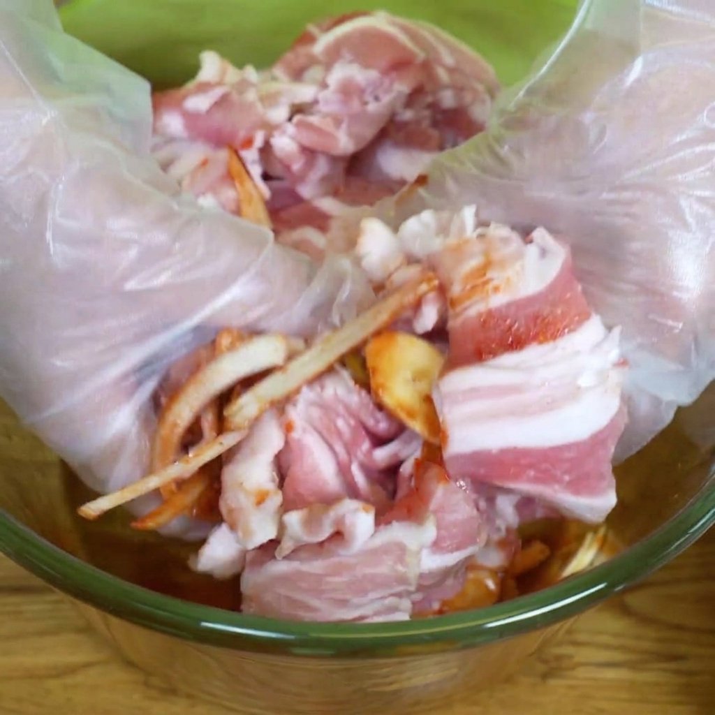 Hände in Einweghandschuhen vermengen das Fleisch mit der Marinade.