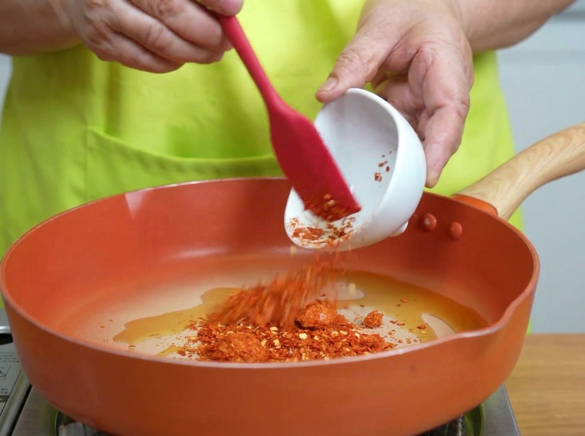 Chiliflocken werden im schimmernden heißen Öl in der Pfanne verrührt.