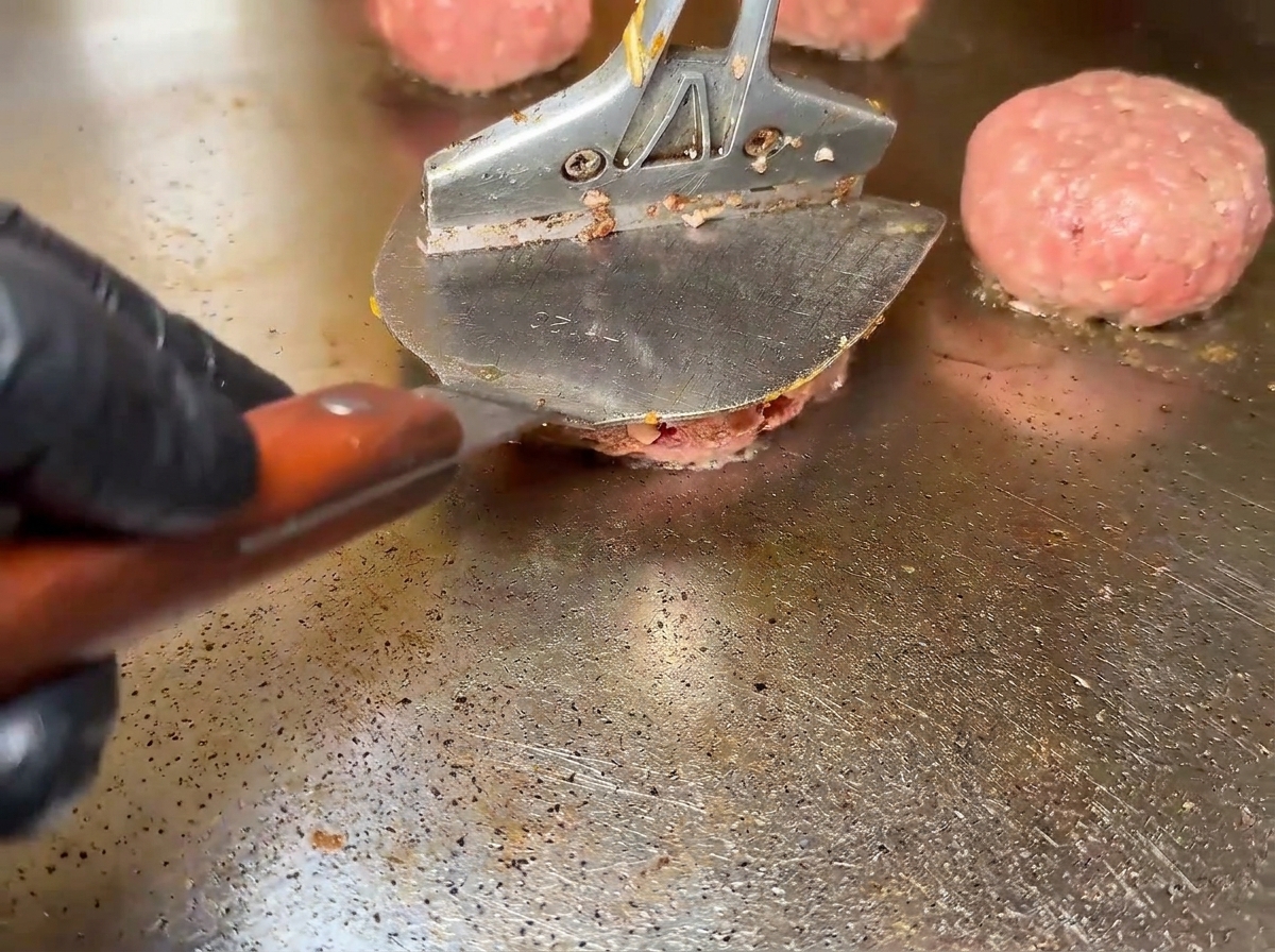 Raw beef patties sizzling on a hot griddle surface.