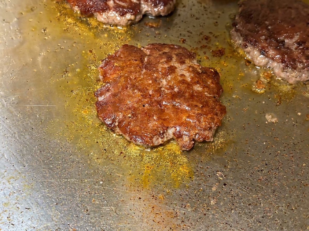 Close-up of melty cheese draped over seared beef patties on the griddle.