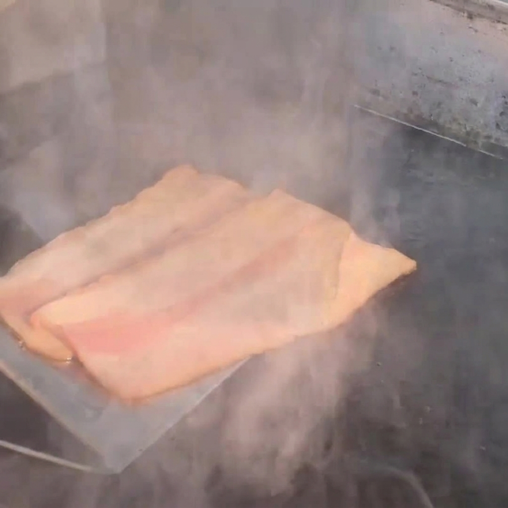 Speckstreifen braten auf einer heißen Platte und geben Dampf ab.