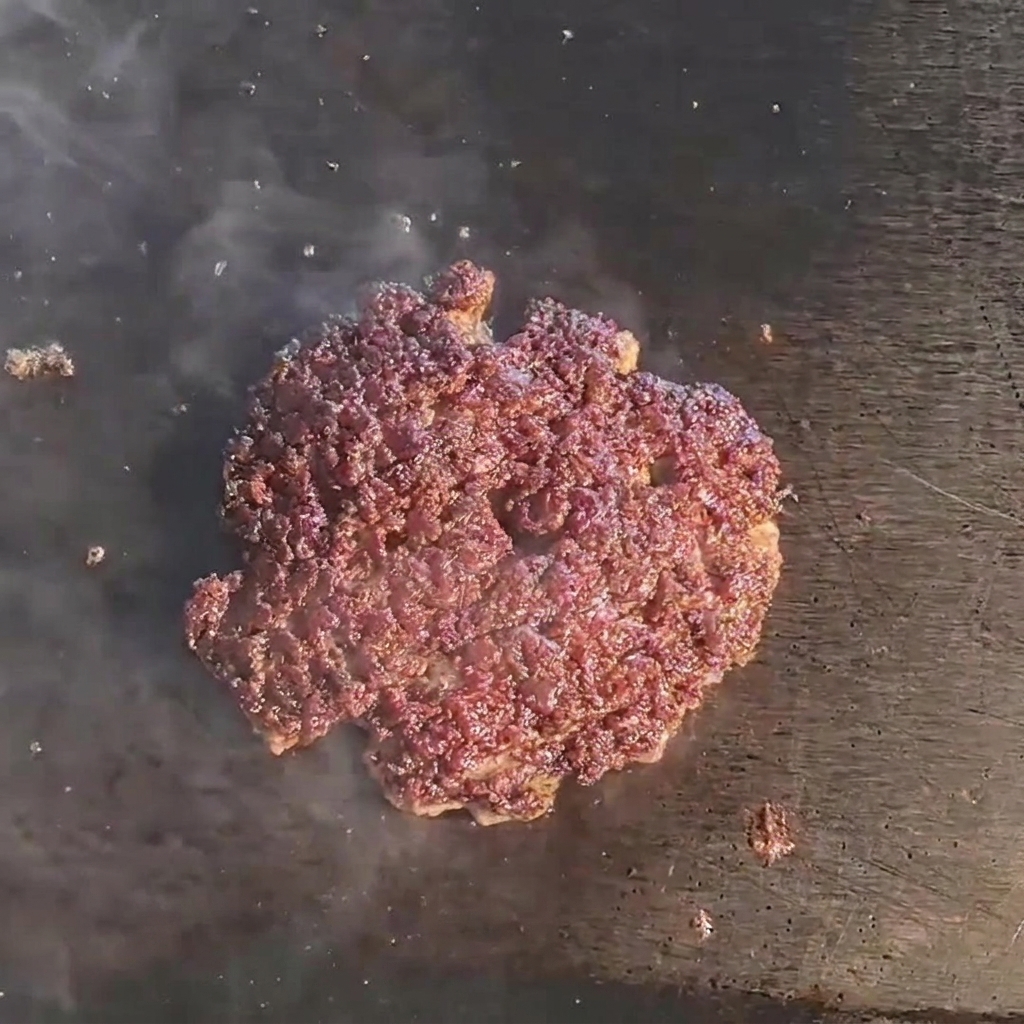 Eine schmelzende Käsescheibe liegt auf einem gebräunten, saftigen Rindfleisch-Patty auf dem Grill.