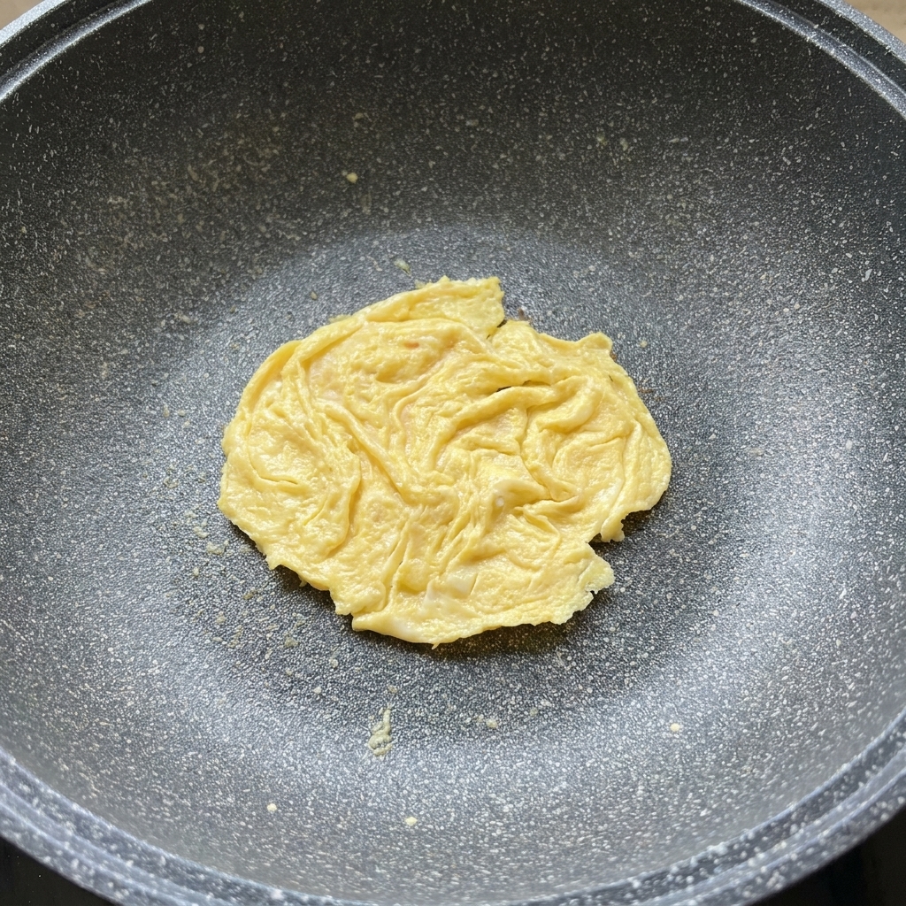 Eine Scheibe Käse, die auf einem gegarten Eipancake in einer Pfanne schmilzt.
