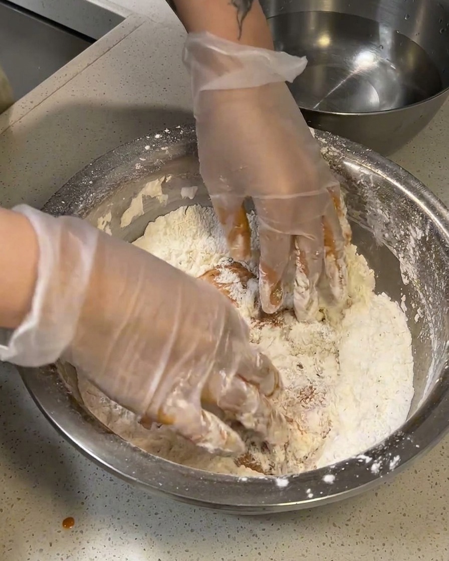 Mariniertes rohes Hähnchen wird fest in eine Schüssel mit trockenem Mehl-Mix gedrückt.