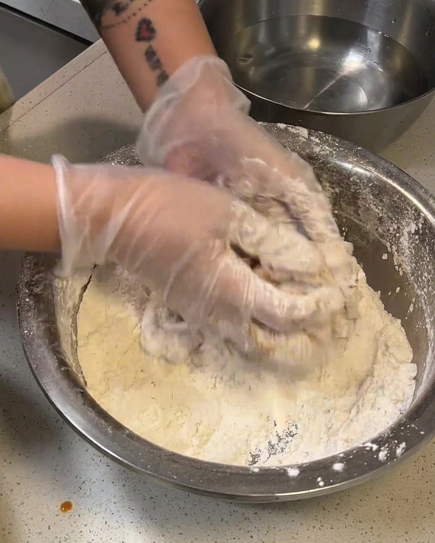 Ein mehliertes Hähnchenfilet wird kurz in eine Schüssel mit Wasser getaucht.