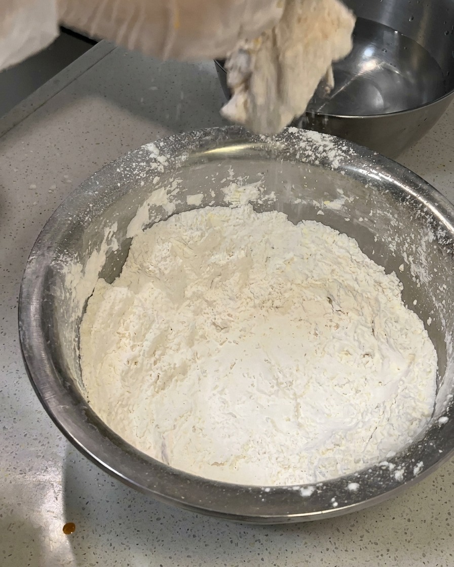 Das panierte Hähnchenfleisch wird vorsichtig mit mehr Mehl bestreut, um eine flockige Kruste zu bilden.