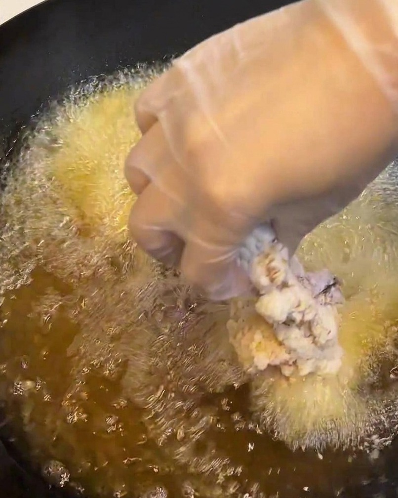 Ein paniertes Hähnchenfilet wird in eine Pfanne mit heißem, sprudelndem Öl gelegt.