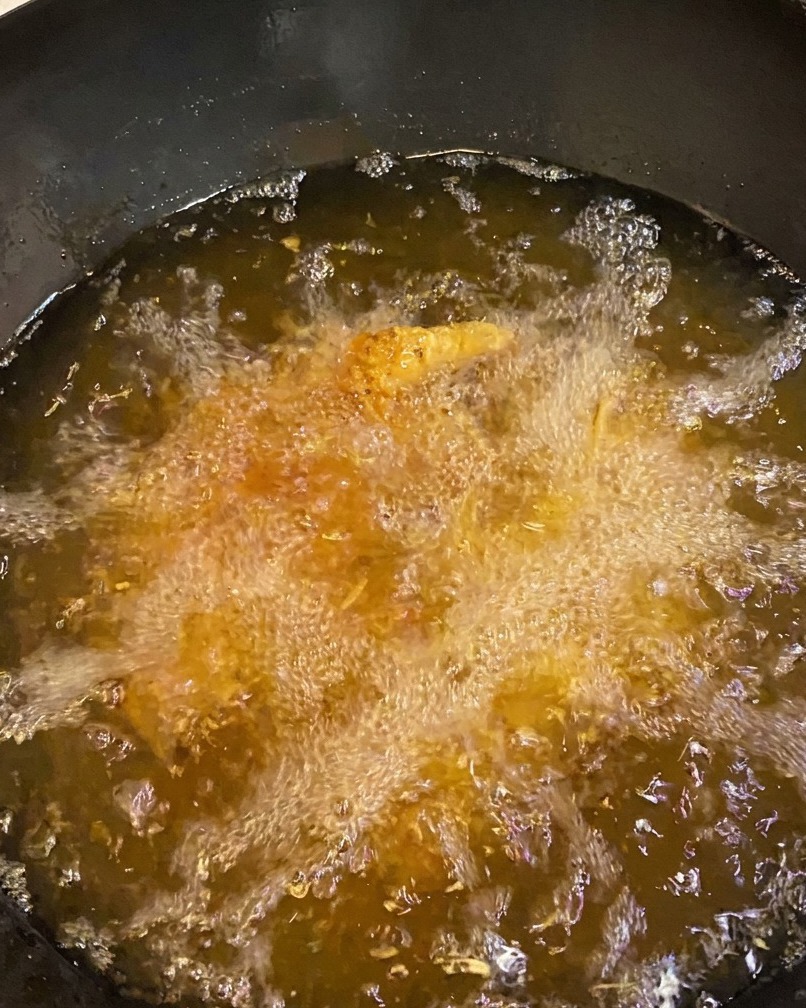 Hähnchenschenkel frittieren in tiefem Öl und zeigen eine tiefgoldene, knusprige Kruste.