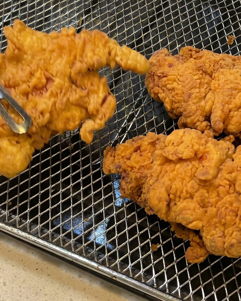 Frittierte Hähnchenfilets werden mit einer Metallzange aus dem Öl gehoben.