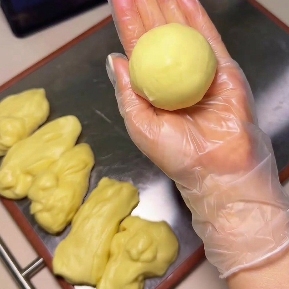 Eine Hand taucht eine Teigkugel in eine Schüssel mit Sesamsamen.