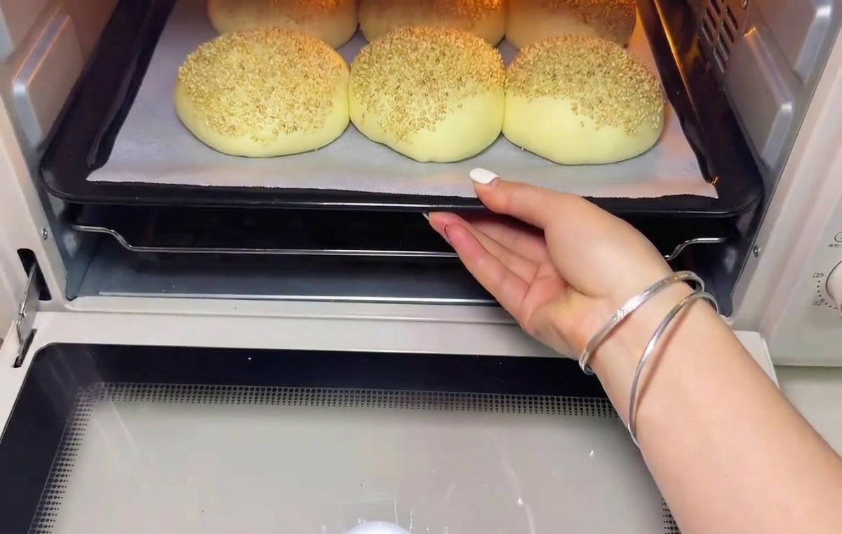 Ein Blech mit aufgegangenen Brötchen wird in den Ofen geschoben.