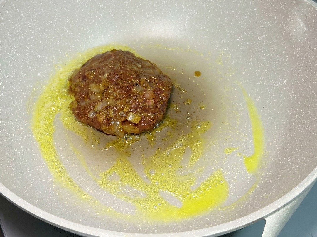 Ein Patty brät in einer Pfanne bei niedriger Hitze.