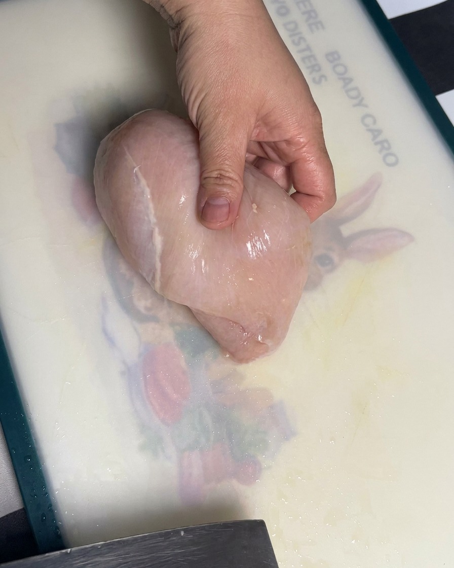 Rohes Hähnchenbrustfilet wird auf einem Schneidebrett in gleichmäßige Stücke geschnitten.