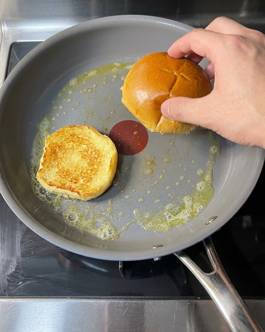 Burgerbrötchen in einer Pfanne mit geschmolzener Butter beim Rösten.
