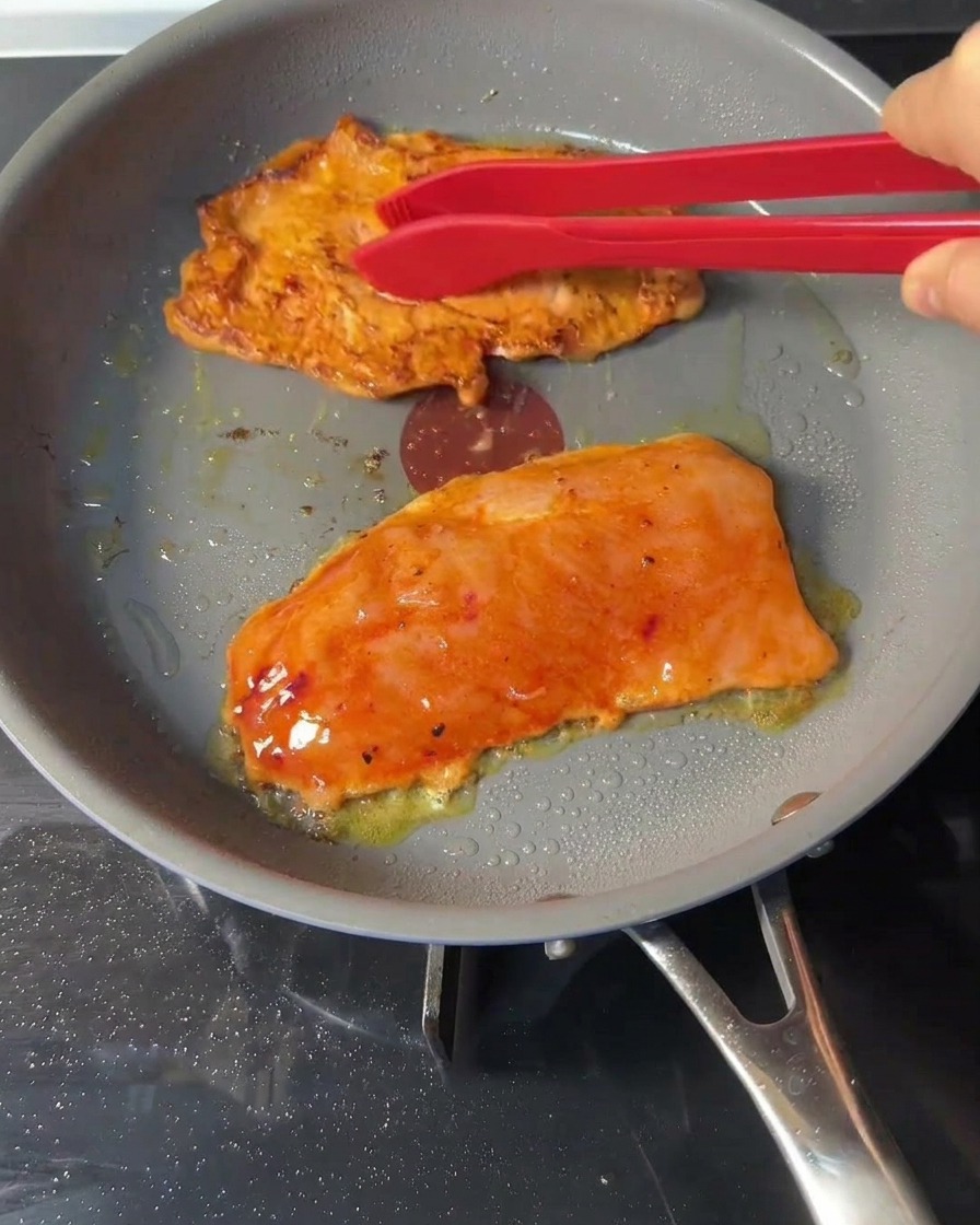 Hähnchen-Patties werden mit einer roten Grillzange in der Pfanne gewendet.