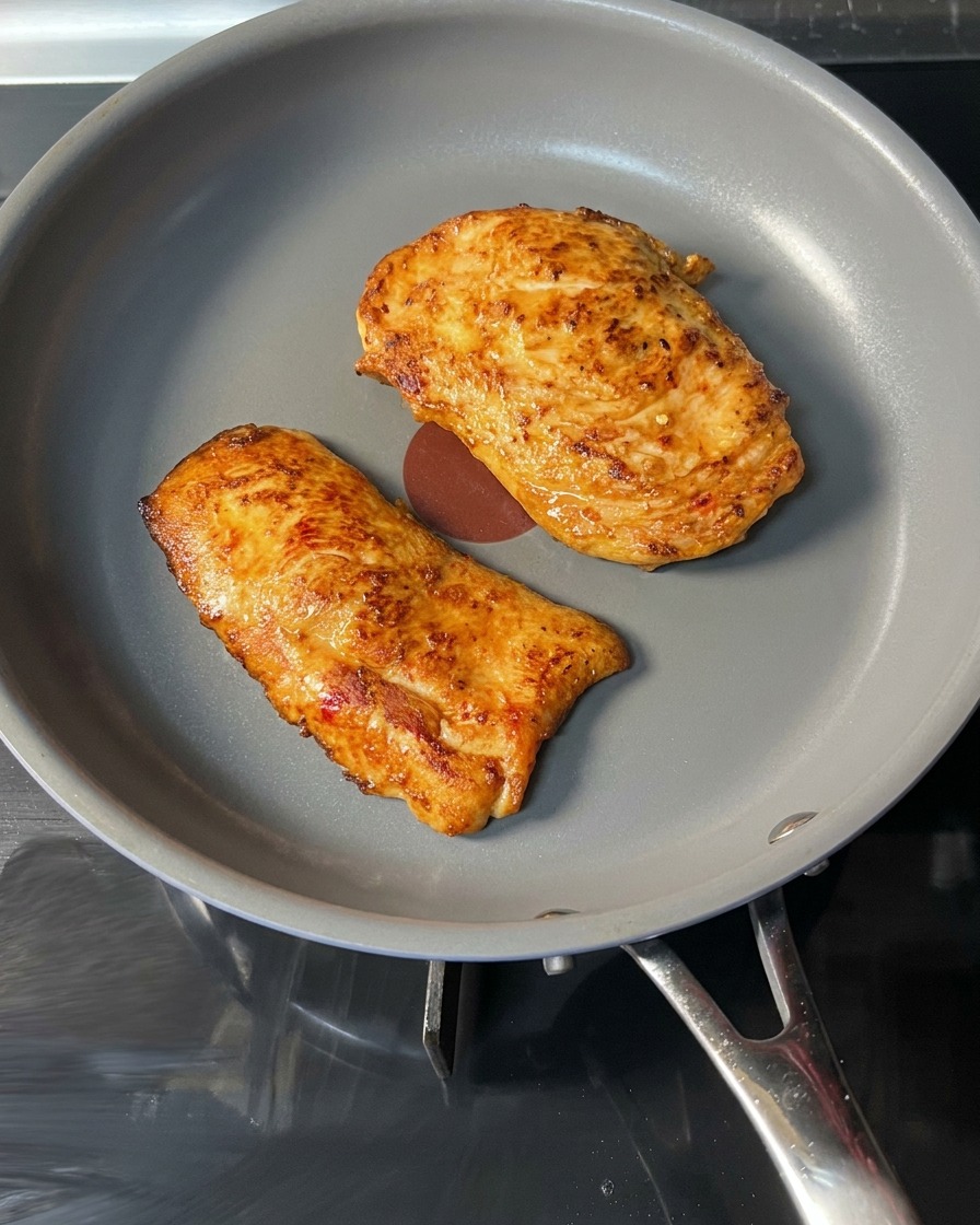 Ein fertiges, goldbraunes Hähnchen-Patty wird mit der Zange aus der Pfanne gehoben.