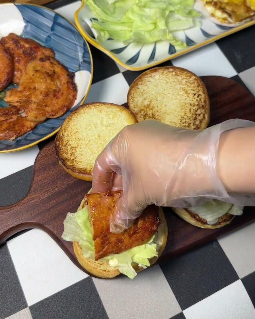 Ein Hähnchen-Patty wird auf ein Salatblatt auf dem Brötchen platziert.