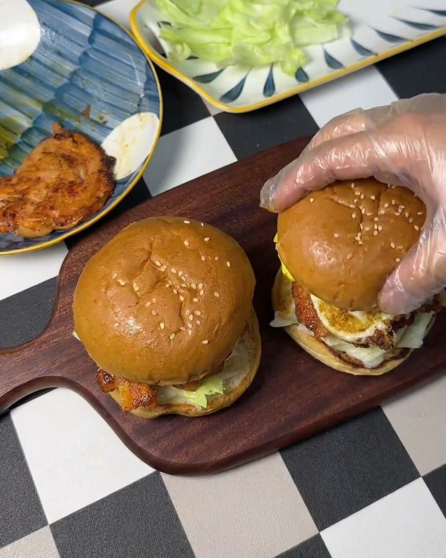 Das Oberteil des Brötchens wird auf den gestapelten Burger gesetzt.