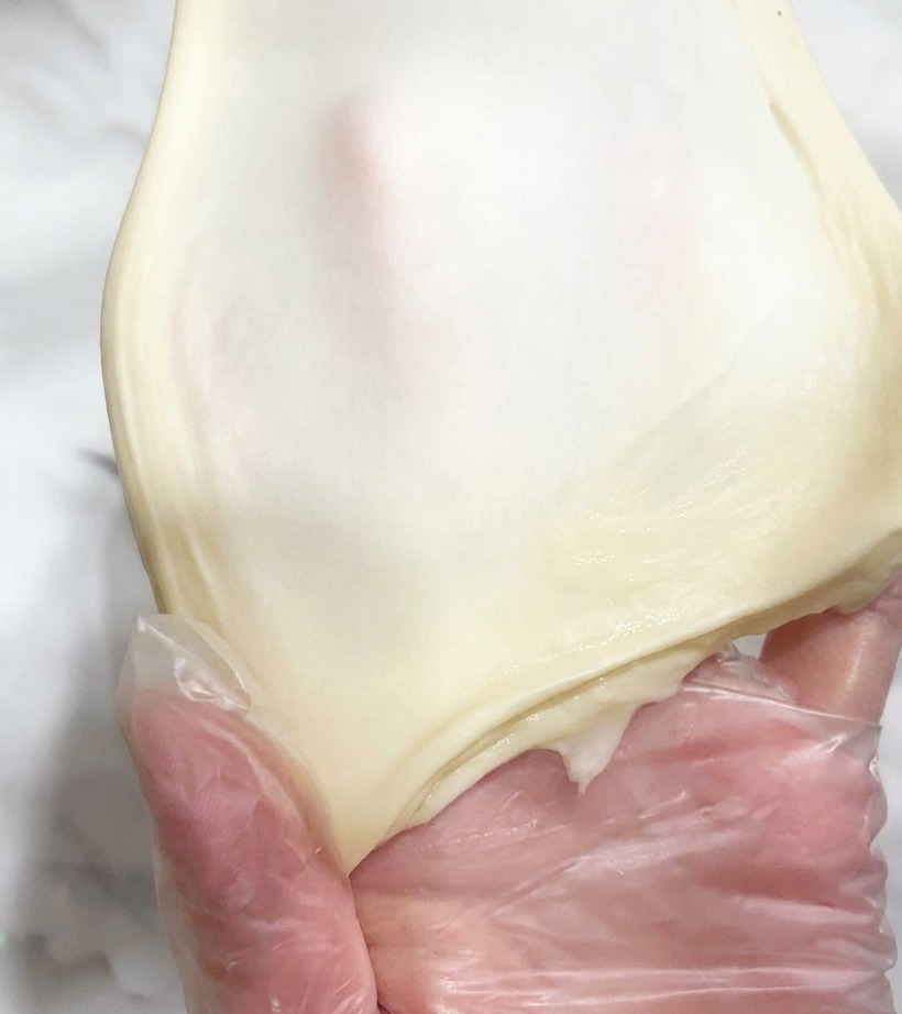 Ein Stück elastischer Teig wird dünn auseinandergezogen.