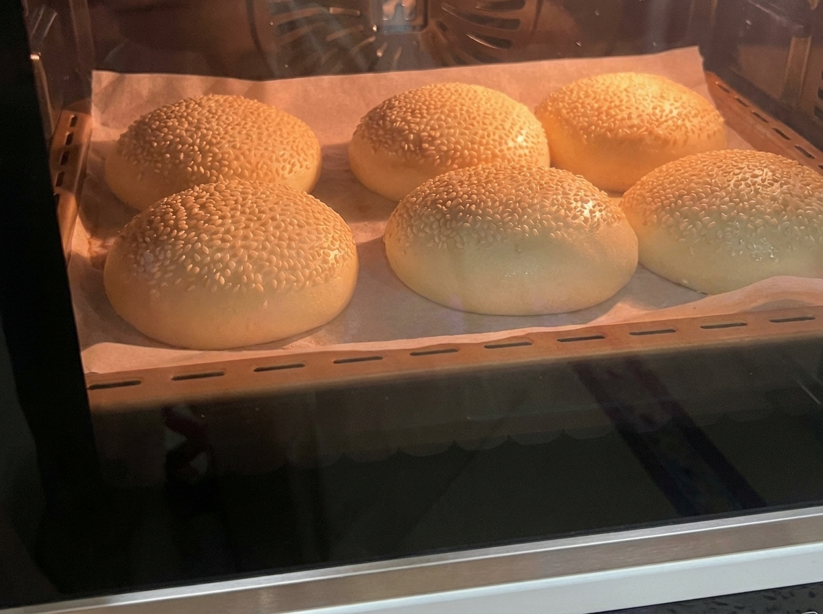 Frisch gebackene, goldbraune Sesam-Brötchen auf einem Blech.