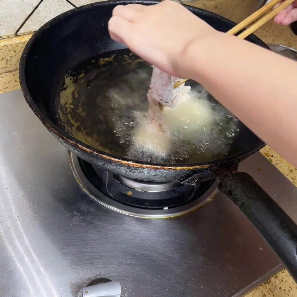 Hähnchen wird vorsichtig in heißes Öl gegeben.
