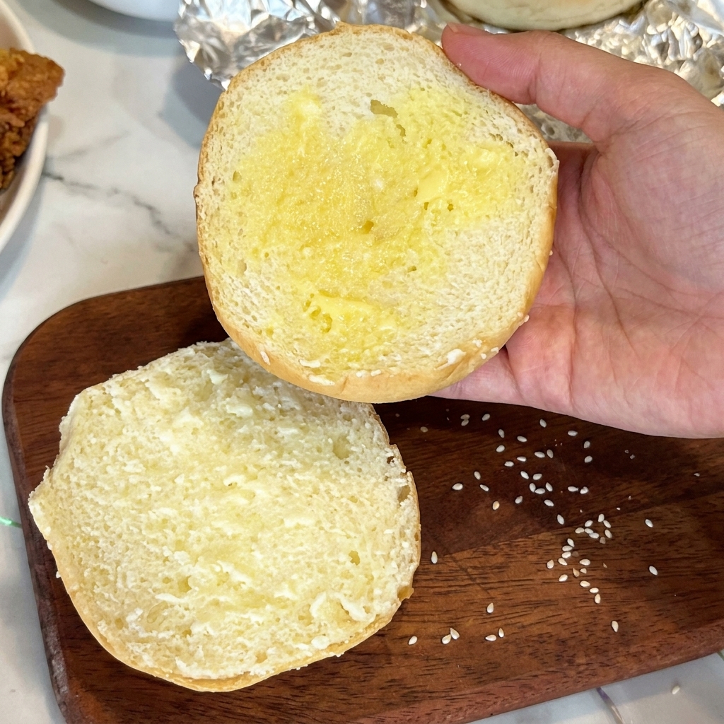 Die Innenseite eines Brötchens wird mit Butter bestrichen.