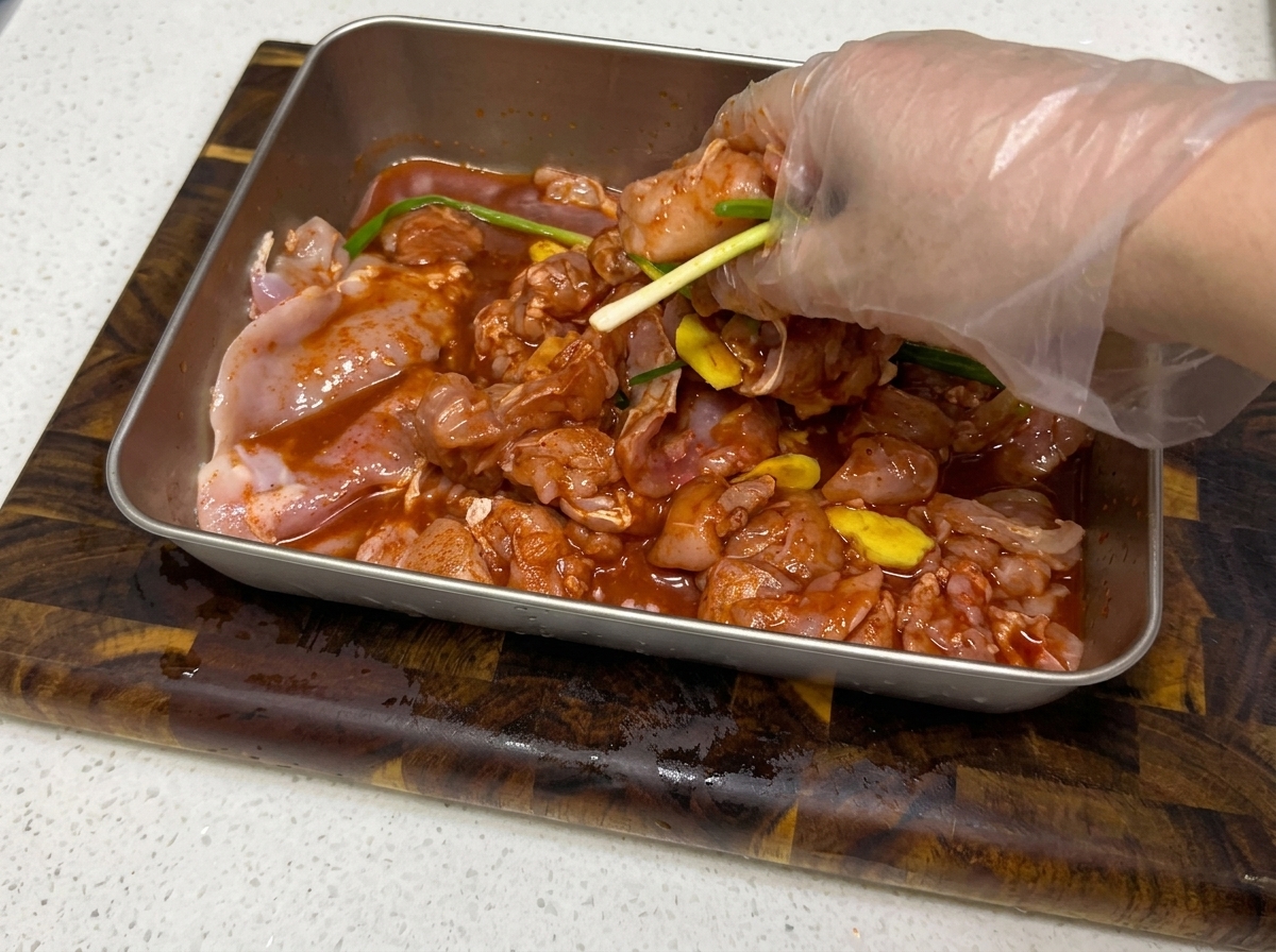 Hände massieren die Marinade in die Hähnchenstücke in einer Metallschale ein.
