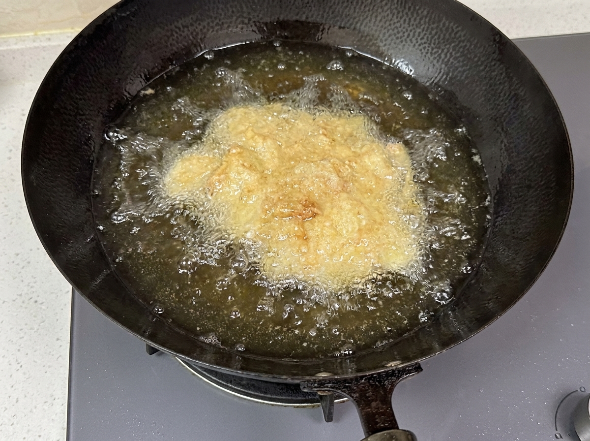 Panierte Hähnchenstücke sprudeln in heißem Öl in einem dunklen Wok.
