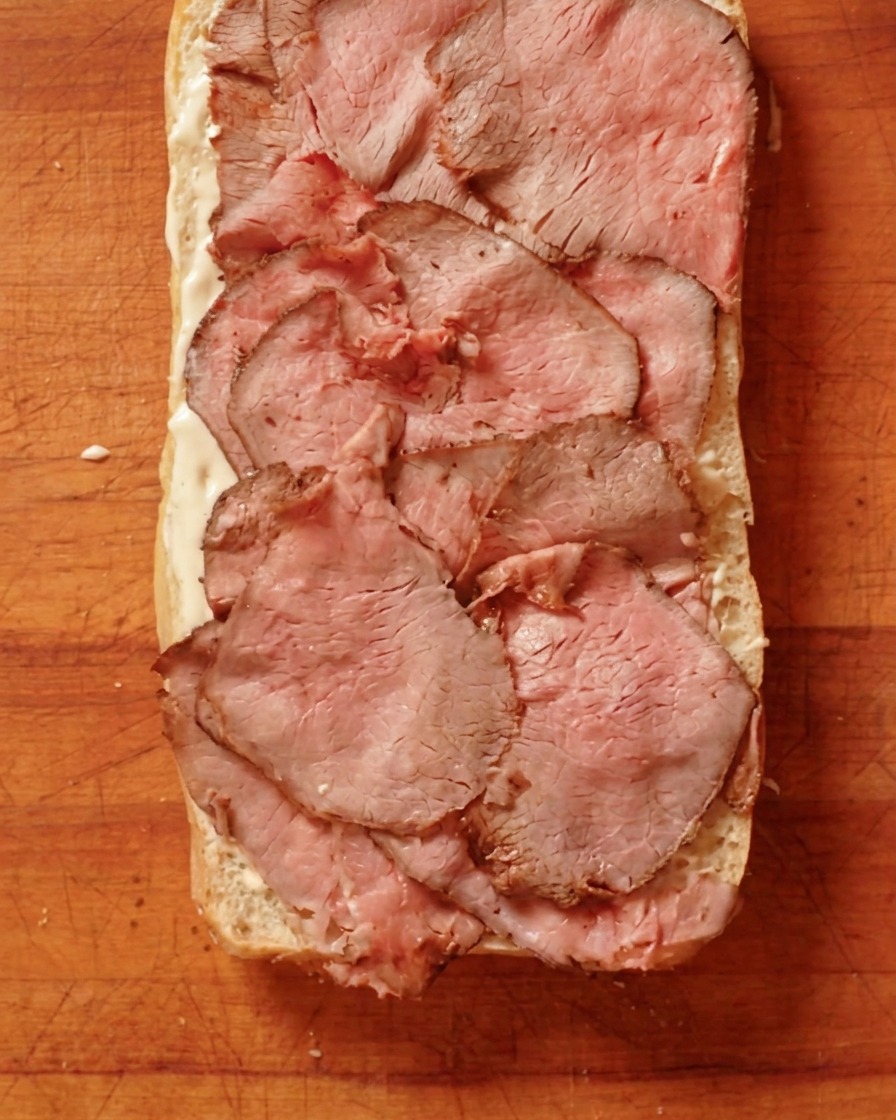 Dünn aufgeschnittenes Roastbeef wird auf dem bestrichenen Brot arrangiert.
