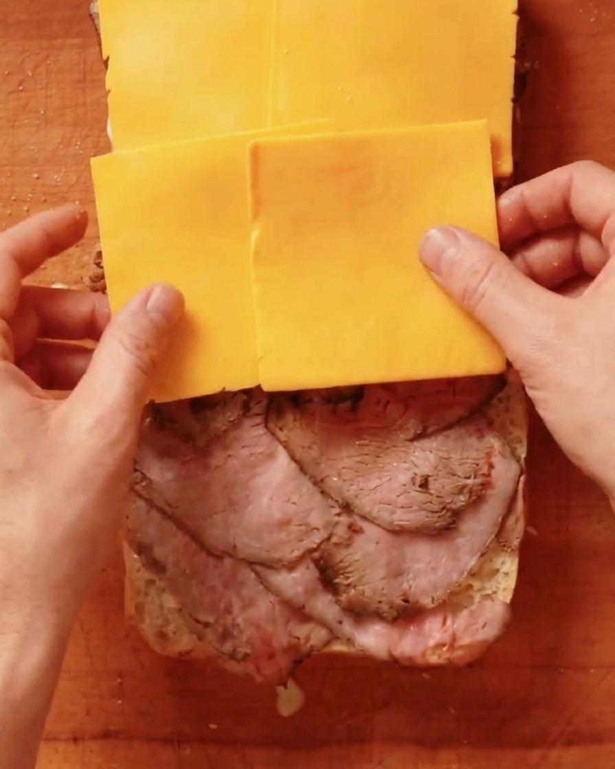 Scheiben von gelbem Cheddar-Käse werden auf das Roastbeef gelegt.