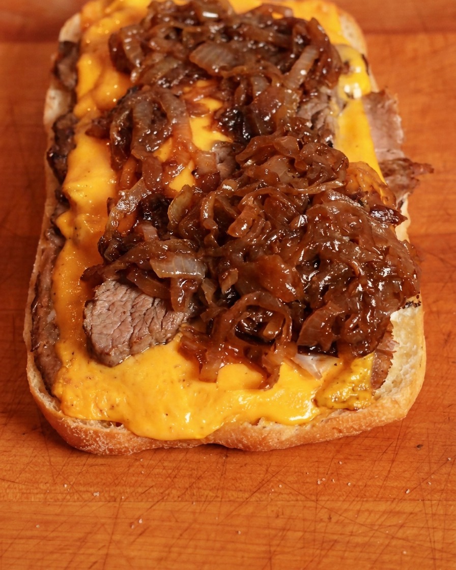Dunkle, karamellisierte Zwiebeln werden über den Cheddar-Käse gegeben.