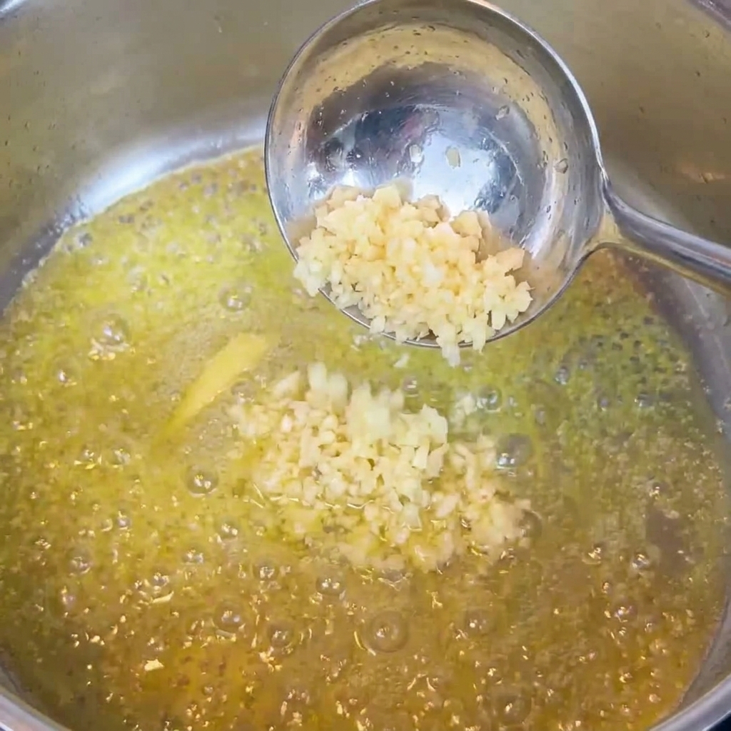 Gehackter Knoblauch wird in geschmolzener Butter in einer Pfanne gerührt.