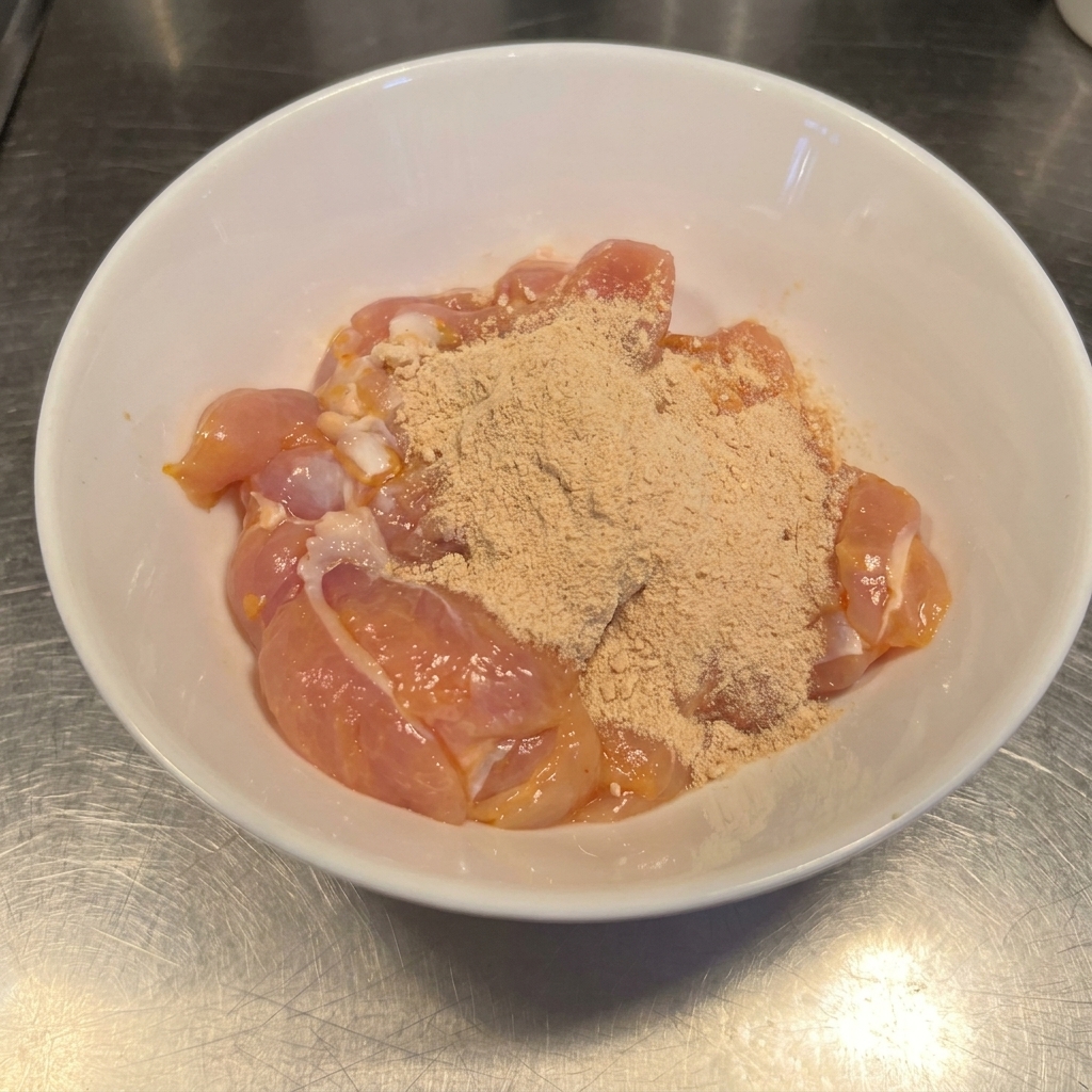 Rohe Hähnchenschenkel in einer Schüssel, bestäubt mit rötlich-braunem Chilipulver und Knoblauchgewürz.