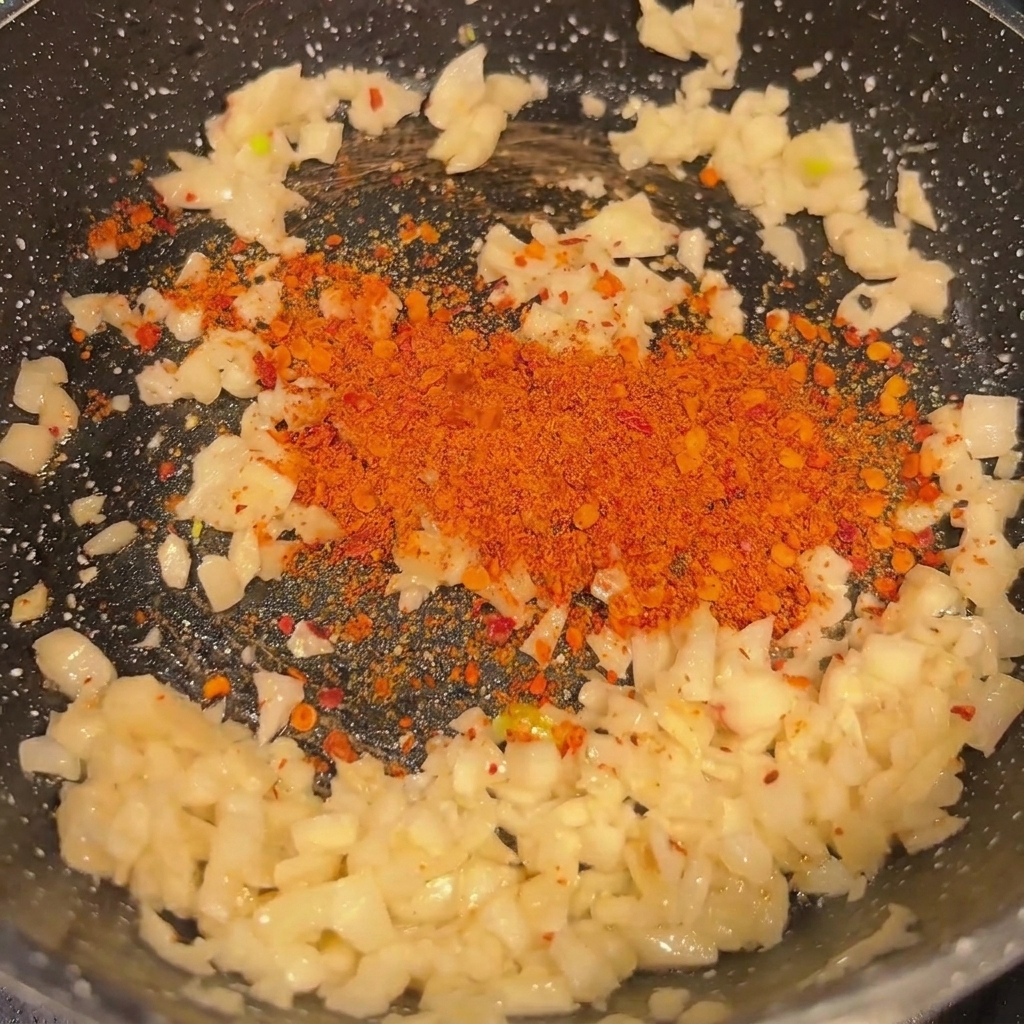 Gehackter Knoblauch und Chilipulver werden in einer Pfanne angebraten.