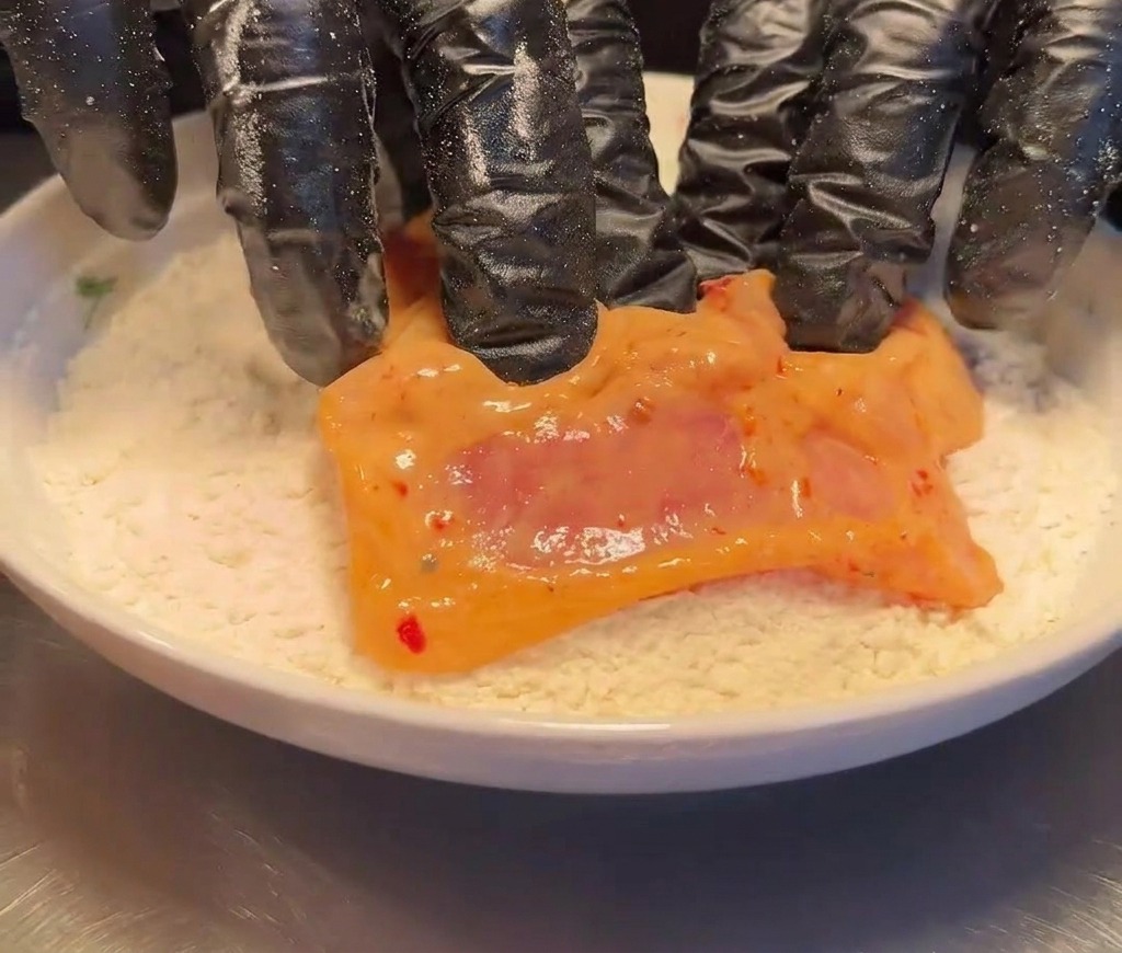 Ein mariniertes Hähnchenstück wird in einer Schüssel mit Mehl gewendet.