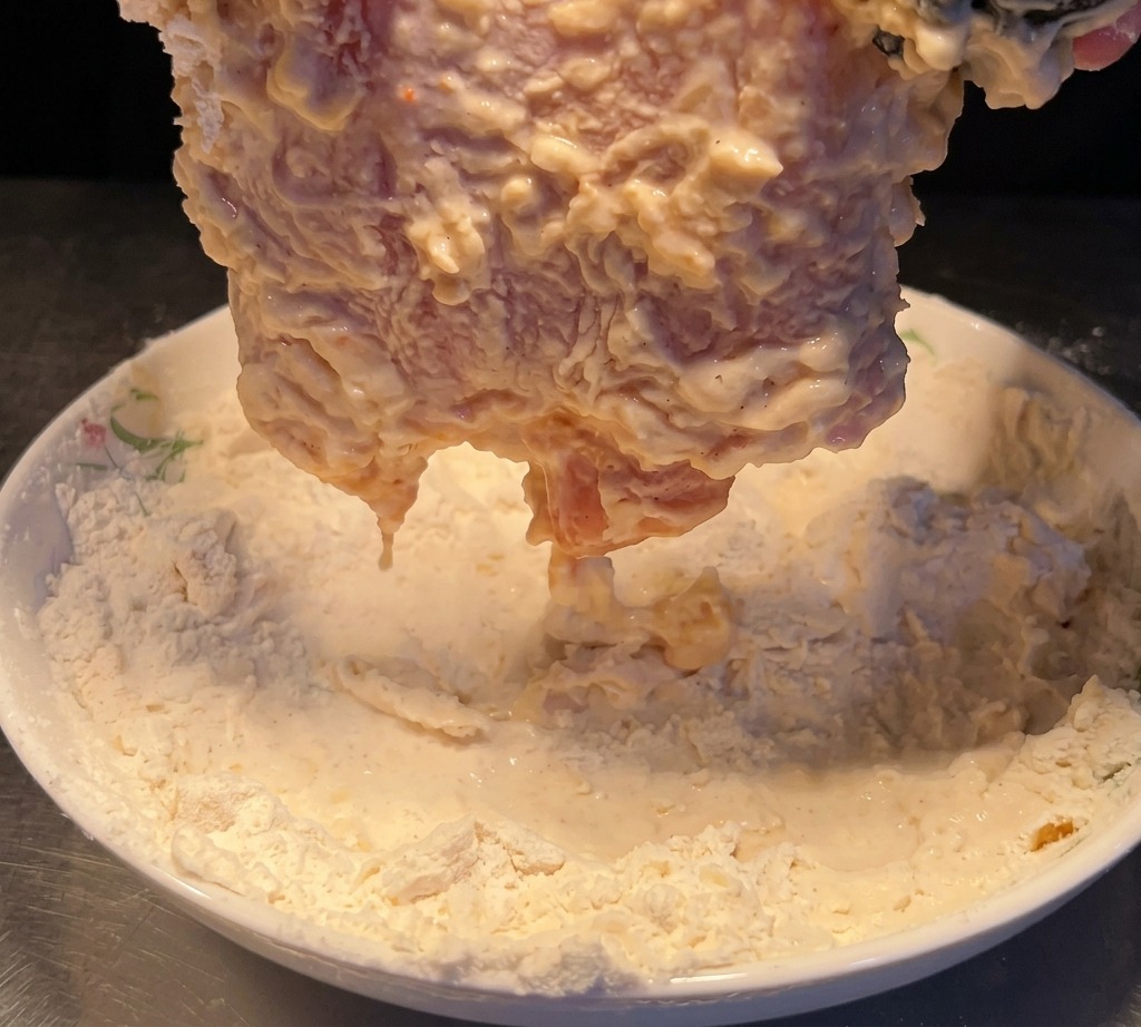 Das befeuchtete Hähnchenstück wird erneut in Mehl gedrückt.