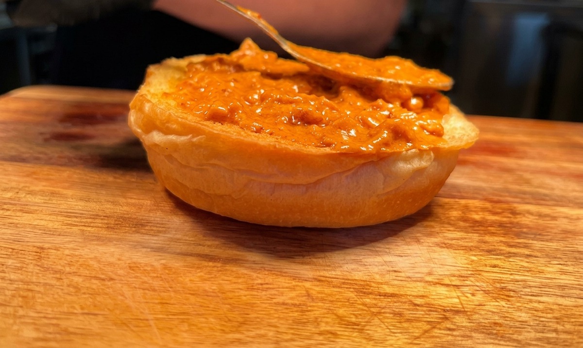 Ein Löffel verteilt Sauce auf einer gerösteten Burger-Brötchenhälfte.
