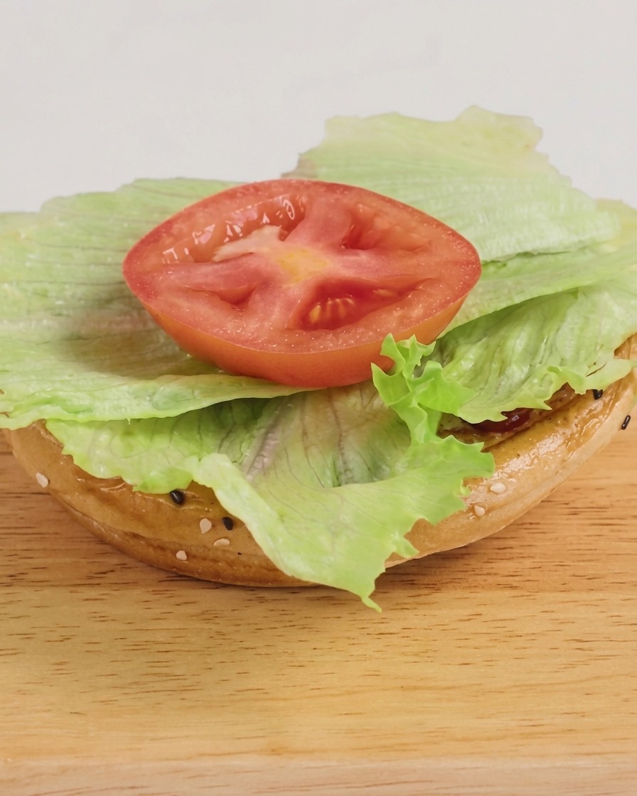 Ein frisch zusammengesetzter Burger mit Salat, einem käsigen Rinderpatty und einem Klecks BBQ-Sauce, servierfertig.