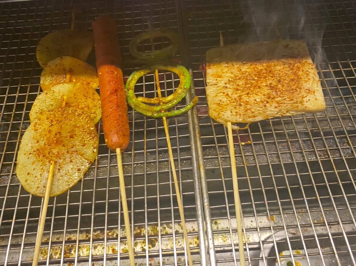Gegrillte Kartoffelscheiben, Wurst und Gemüse, überzogen mit glänzender Barbecue-Sauce und Chiliflocken.