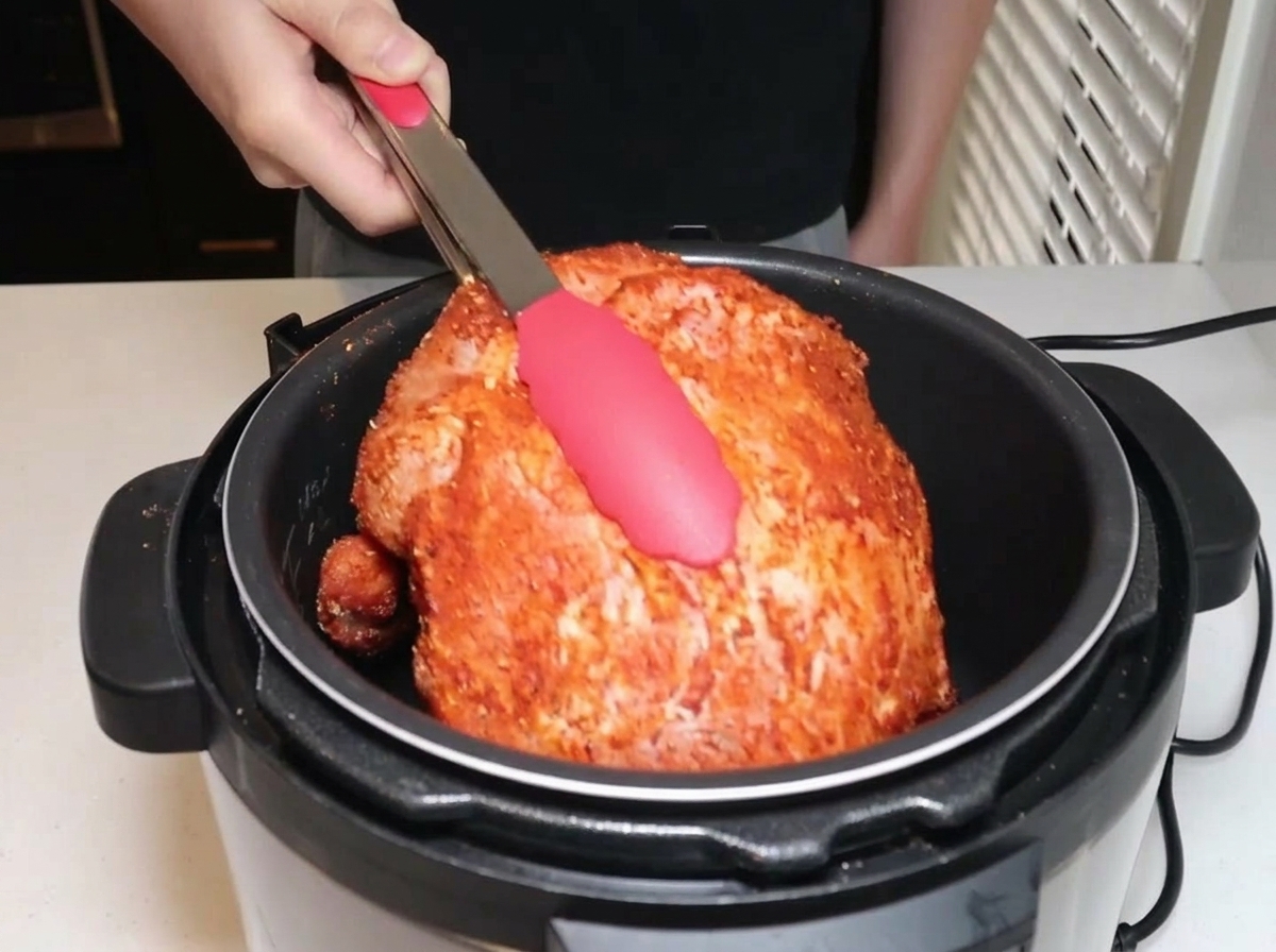 Gewürzte Schweineschulter wird mit einer Zange in einen elektrischen Schnellkochtopf gelegt.